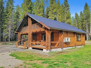 A wooden cabin with a porch, a chimney, and a window with an air conditioning unit.