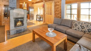 A cozy log cabin interior with a stone fireplace, wooden furniture, and a view through large windows. - Paloniemi by Interhome (Savitaipale)