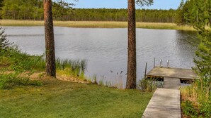 A wooden dock leading to a small wooden pier over a calm lake, surrounded by trees and grassy areas. - Paloniemi by Interhome (Savitaipale)