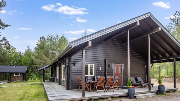 A cabin with a covered porch, a dining area with wooden furniture, and a large potted plant.