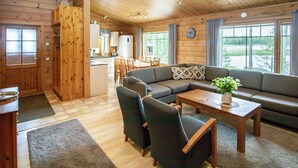 Un interior de cabaña acogedor, con sala de estar, sofá, sillas, una mesita de centro y una cocina al fondo.