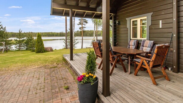 Una terraza de madera con una mesa y sillas, con vista a un lago.