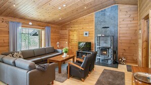 Un acogedor interior de cabaña con paredes de madera, una chimenea, un sofá, un televisor y un comedor.