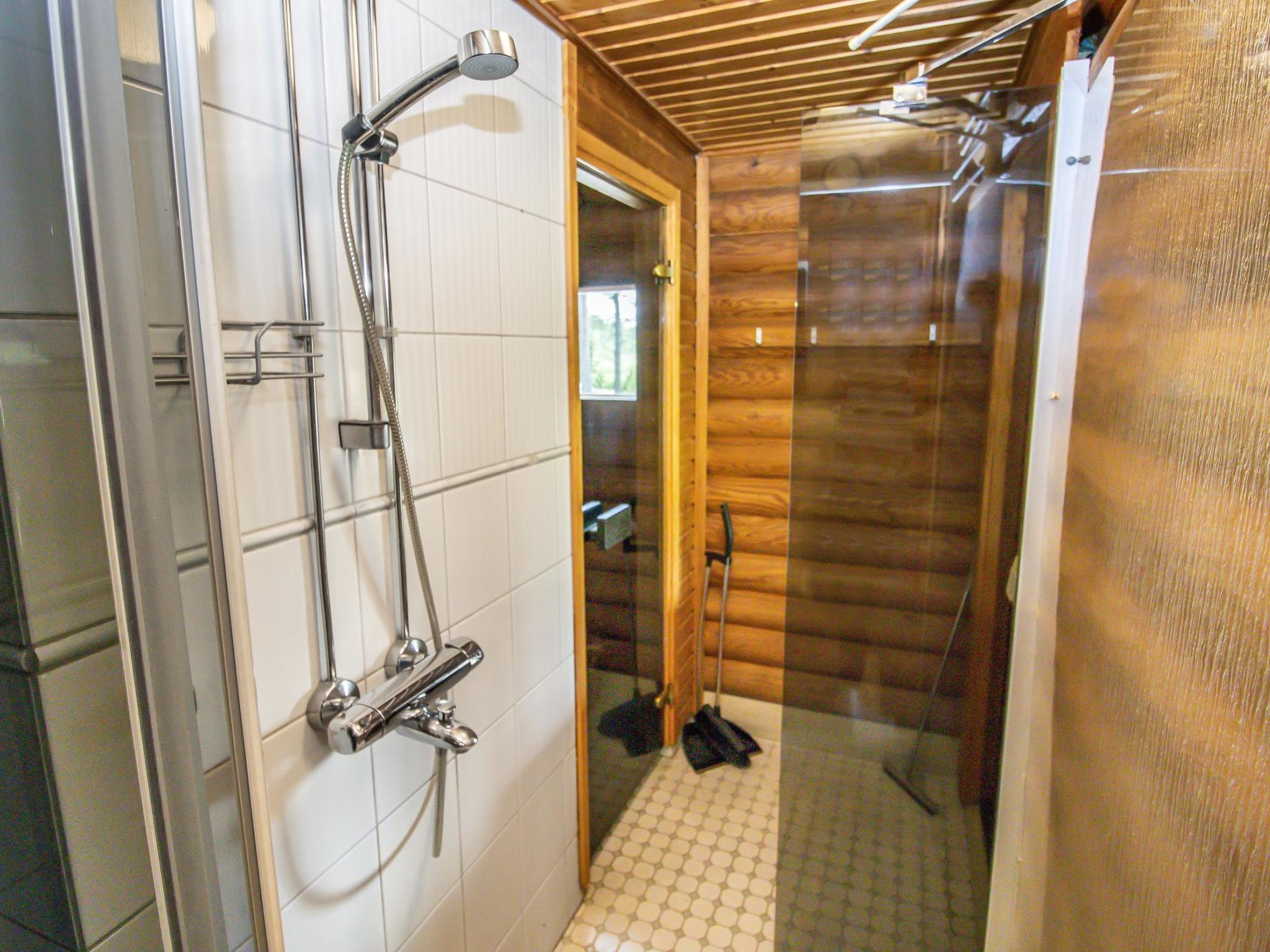 A shower area with a glass door, wooden walls, and a tiled floor.
