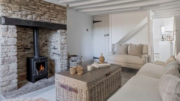 Un salon chaleureux avec une cheminée en pierre, une table basse en osier et un canapé beige.