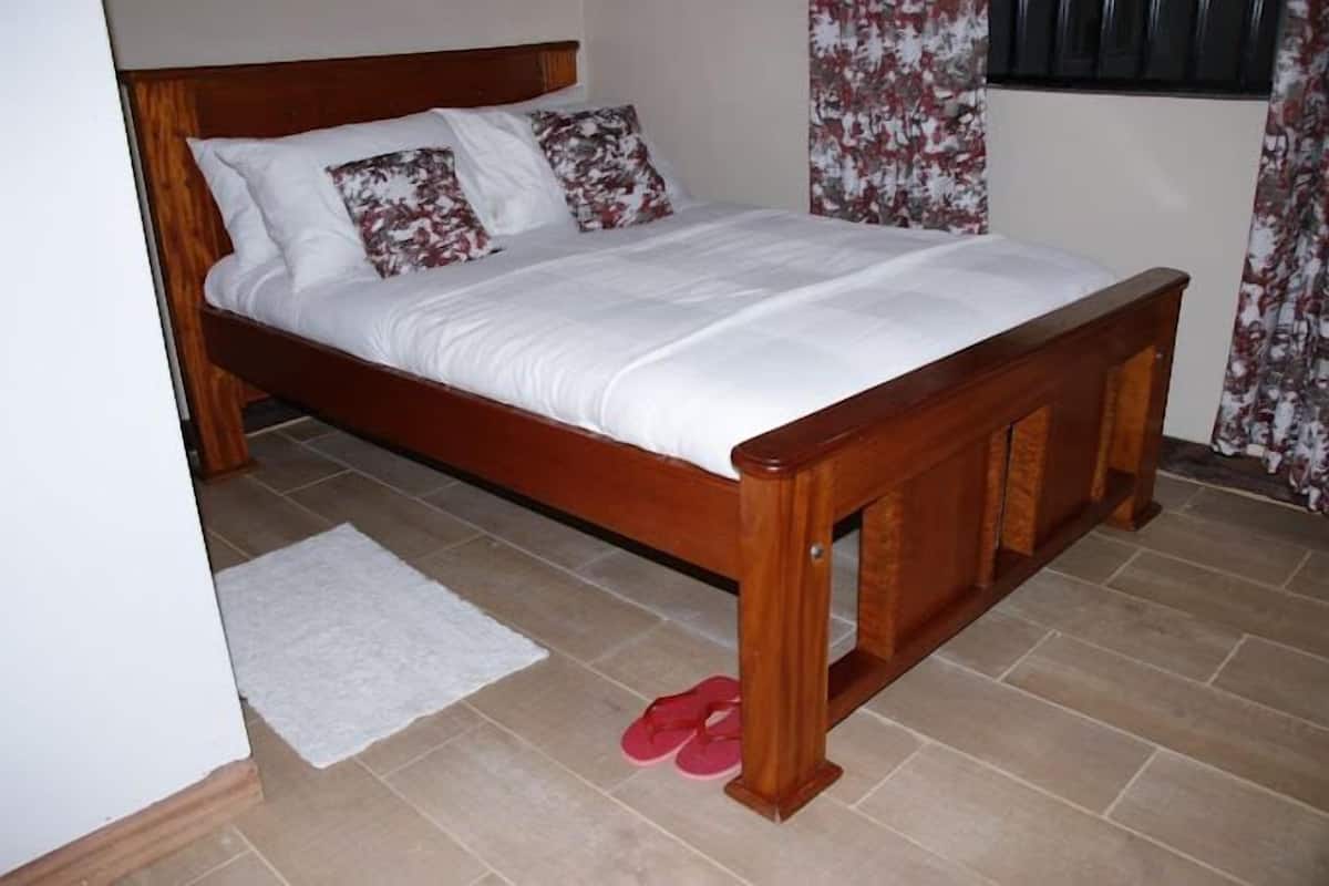 A wooden bed with white bedding and floral pillows in a room with tiled flooring and a white rug.