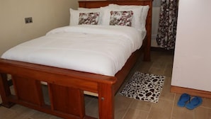 A neatly made bed with a wooden frame, white bedding, and floral-patterned pillows. - Kimberly Guest House Naivasha (Naivasha)