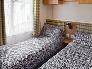 A small, single-room accommodation with two beds, a window with curtains, and a wooden headboard.