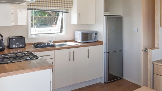 A compact kitchen with a gas stove, a microwave, a refrigerator, and a sink. - Seaview Two - UK50166 (Corton)