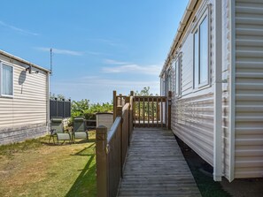 Een houten terras leidt naar een stacaravan met een omheinde achtertuin.