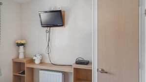 A bedroom with a bed, a mounted TV, a radiator, and a shelf with a vase and a remote control. - Seaview Two - UK50166 (Corton)