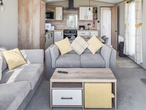 Un espacio habitable compacto con un sofá gris, una mesa de centro de madera y una kitchenette al fondo.