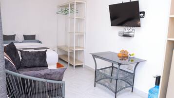 Une chambre d’hôtel moderne avec un lit, un canapé gris, une petite table, une télévision et une armoire.