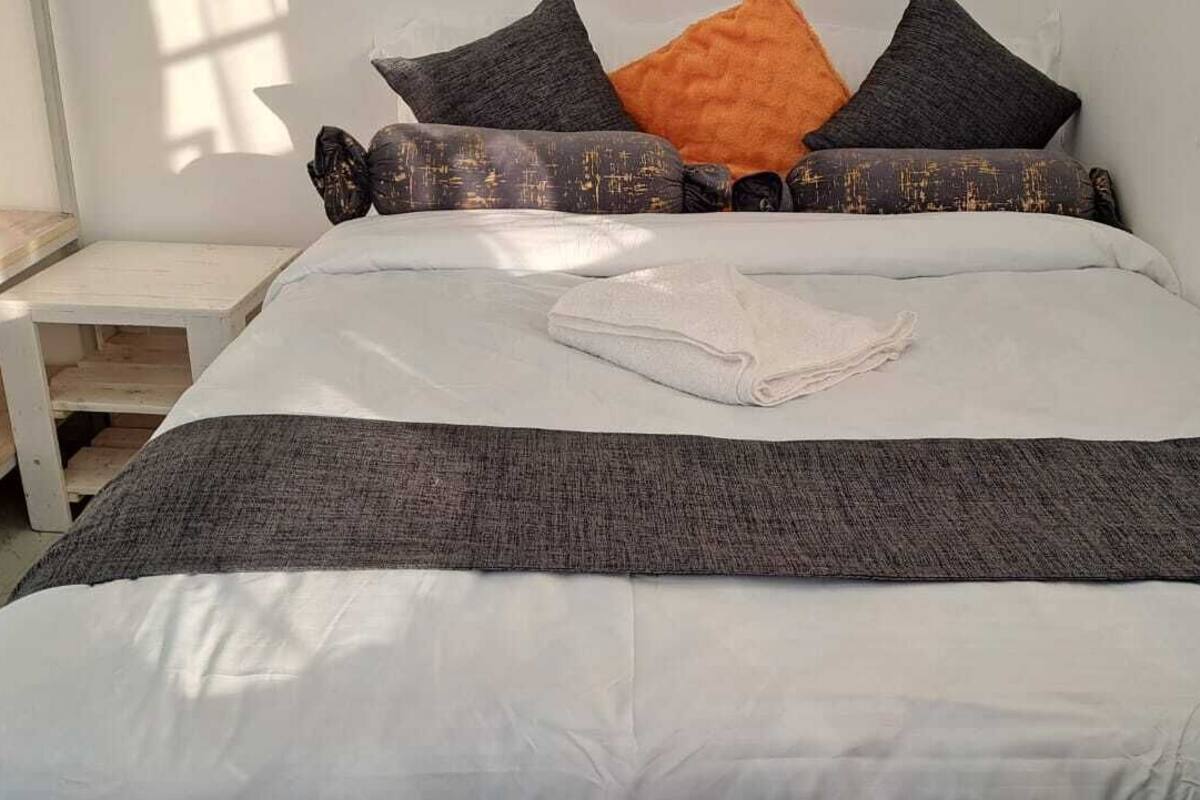 Un lit bien fait, avec une couette blanche, des oreillers aux motifs gris et noirs et une serviette blanche pliée.