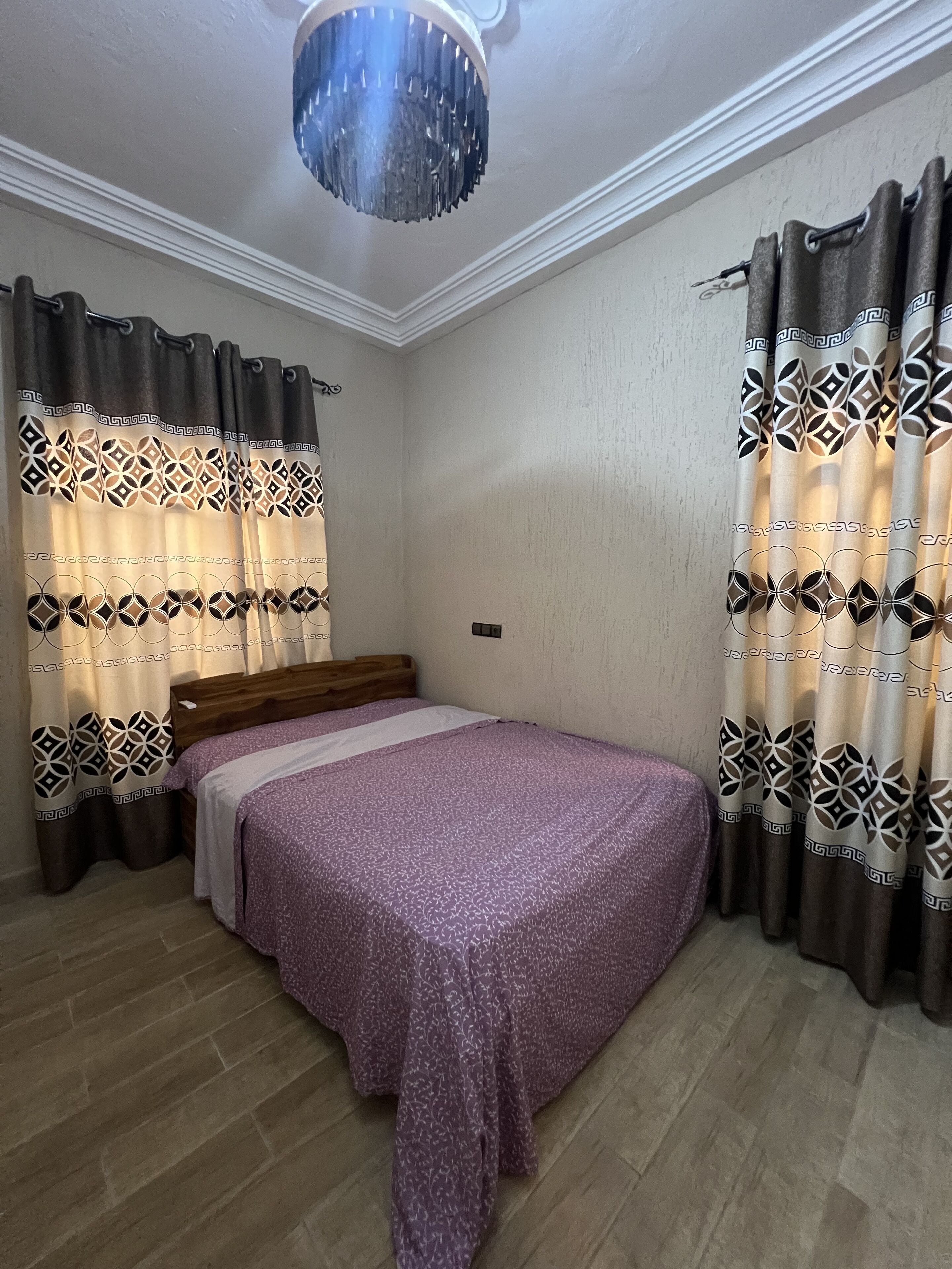 A bedroom with a bed, curtains, a chandelier, and a wooden headboard.