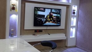 A modern living room with a flat-screen TV mounted on the wall, a white console table, and a black chair. - Le11Onze: 2-Bed, 1-Bath - Apt 2 (Apessito)