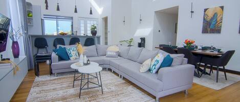 A modern living room with a grey sectional sofa, a round coffee table, and a dining area with a table and chairs.