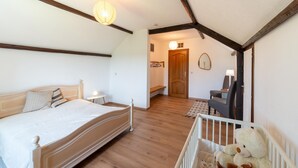 Un dormitorio con cama de madera, una cuna con peluches, un escritorio con silla y una puerta que da a otra habitación.