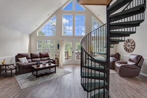 Un salon spacieux avec un plafond haut, un canapé en cuir marron, une table basse et un escalier en colimaçon.