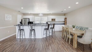 Een moderne keuken met een centraal eiland, barstoelen, een eettafel met stoelen en een koelkast.