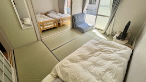 Une pièce de style japonais traditionnel, avec un sol recouvert de tatamis, un futon servant de lit, un lit bas en bois et un fauteuil futon.