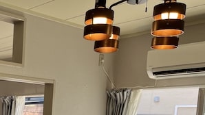 Une pièce avec un grand canapé gris, un climatiseur fixé au plafond et une vue sur l’extérieur grâce à une porte vitrée.