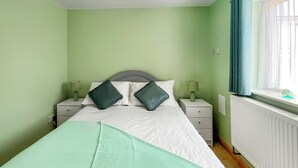 A neatly made bed with a green bedspread, two pillows, and a nightstand with a lamp.