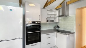 A compact kitchen with white cabinetry, a black oven, a stainless steel refrigerator, and a tiled backsplash.