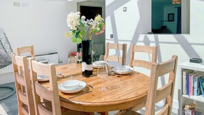 Una mesa de madera redonda con platos blancos, vasos y un florero con flores.