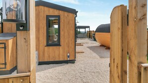 A wooden cabin with a small door and window, a light fixture, and a gravel ground. - Barn Owl Lodge - UK49903 (Dalton, near Wigan)