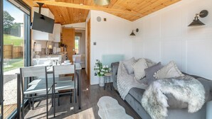 A modern interior with a wooden ceiling, a grey sofa with fluffy pillows, and a dining area with a table and chairs. - Barn Owl Lodge - UK49903 (Dalton, near Wigan)