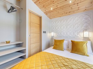Une chambre à coucher avec un lit, une porte en bois, un mur blanc orné de motifs géométriques et une étagère sur laquelle est posé un objet décoratif.