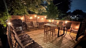 A wooden deck with outdoor furniture, string lights, and a barbecue grill.
