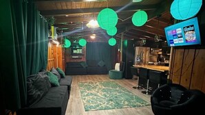 A cozy room with a wooden floor, green curtains, a sofa, a bean bag chair, and a TV displaying 'Goonies'.