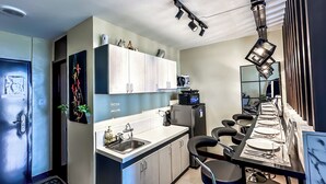 Una cocina moderna con armarios blancos, un lavamanos de acero inoxidable y una zona de comedor con una mesa larga y sillas.