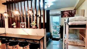 Un espacio habitable compacto con kitchenette, una zona de comedor con taburetes de bar, una cama litera y vistas por una ventana.