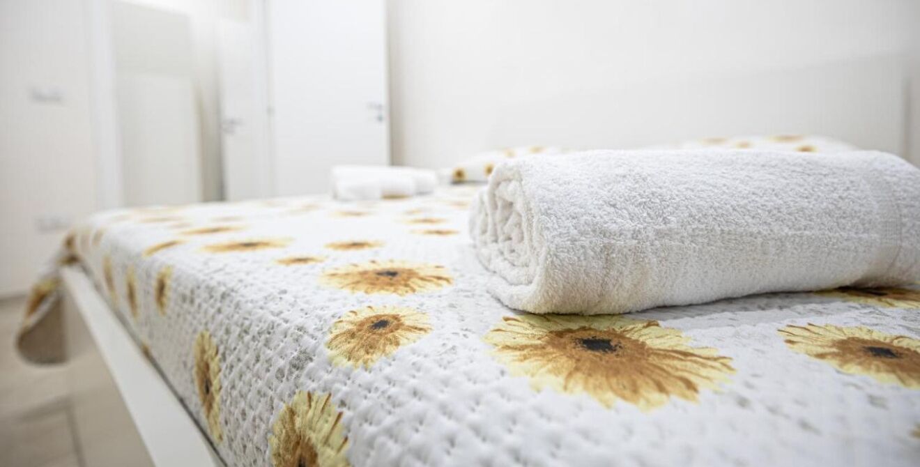 Una cama bien hecha con una colcha estampada de flores y una toalla blanca enrollada encima.