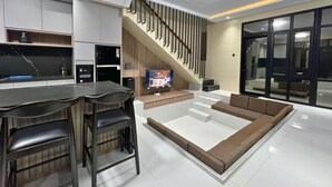 A modern living room with a kitchen area, a flat-screen TV, and a staircase.