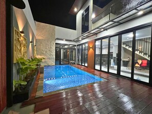 An indoor swimming pool with a tiled floor, surrounded by glass doors and windows, and a staircase leading to an upper level. - Charming 3-bedroom villa with WiFi and AC in fantastic West Java (West Java)