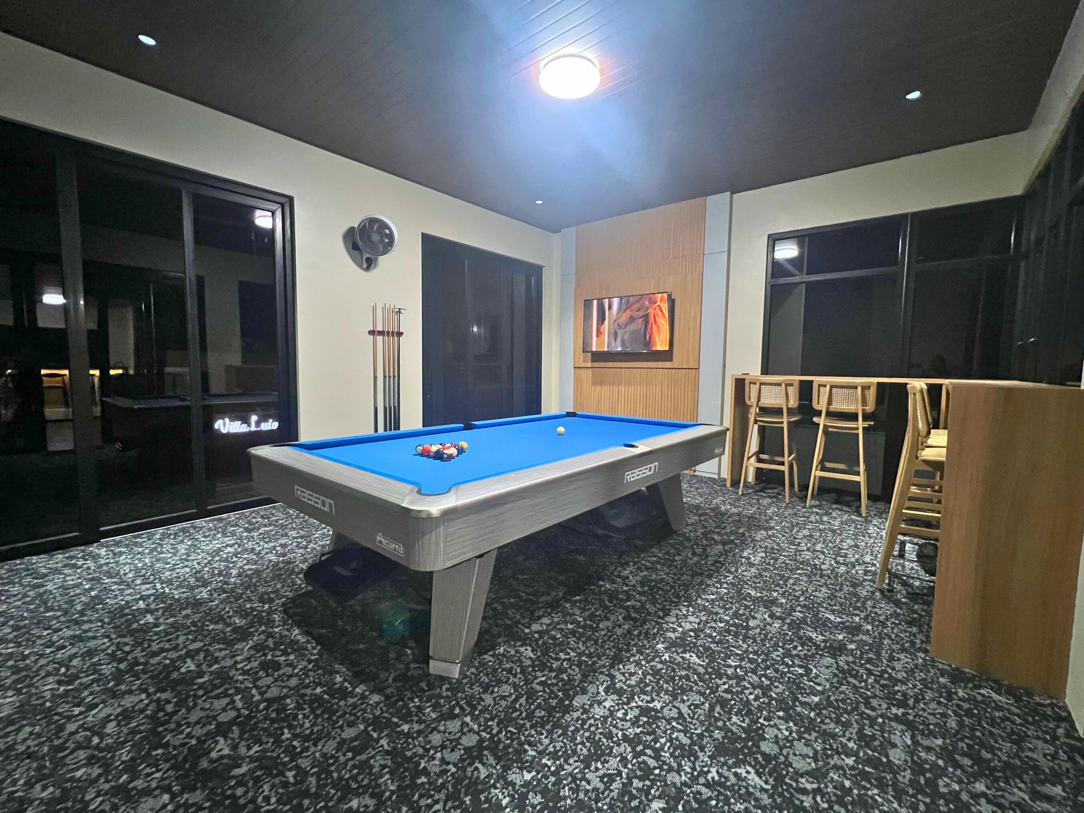 A pool table with a blue felt surface, a ceiling fan, and a billiards rack.