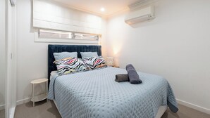 Een slaapkamer met een bed, nachtkastje, lamp en een airconditioning.
