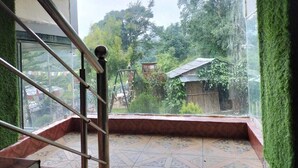 Une pièce dotée d’une grande fenêtre, d’un escalier avec une rampe en métal, et offrant une vue sur un jardin et des bâtiments à l’extérieur.