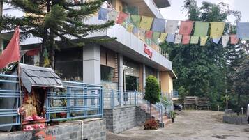 A building with a sign that reads "Hotel". There is a small shrine with a statue and offerings in front of the building.