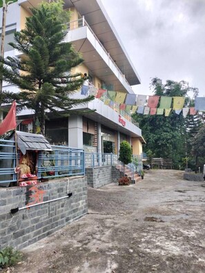 A building with a sign that reads "Hotel". There is a small shrine with a statue and offerings in front of the building. - The Galley (Dharamshala)