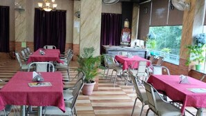 Un restaurant avec de nombreuses tables recouvertes de nappes rouges, des chaises en métal et une plante en pot au centre.