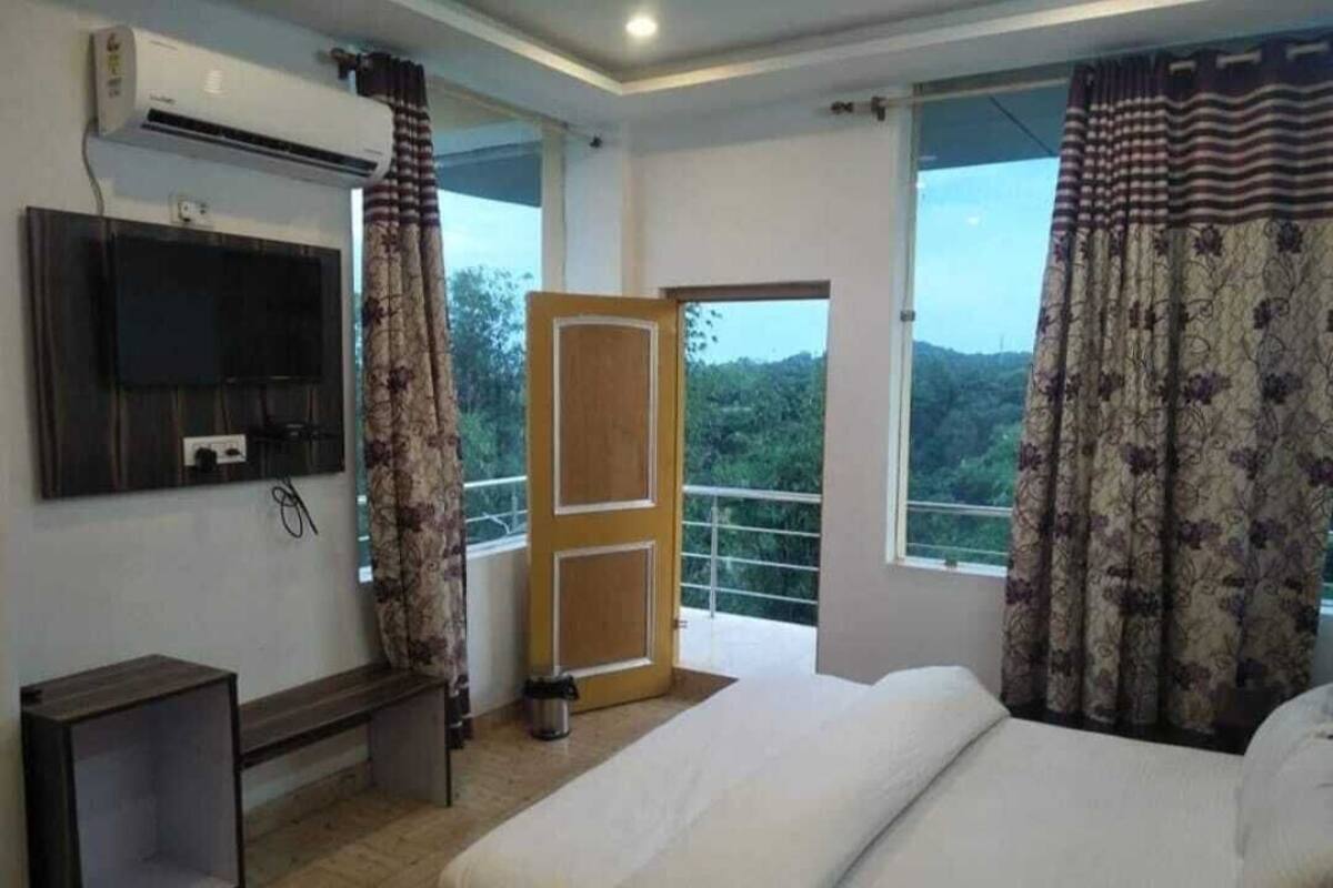 A hotel room with a bed, a TV mounted on the wall, a bench, and a window with curtains.