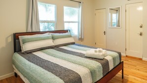 A neatly made bed with striped bedding, a wooden headboard, and a window with curtains.