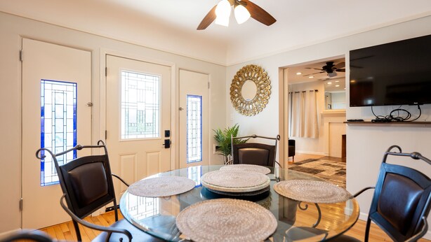 A dining area with a glass table, black chairs, and a ceiling fan.