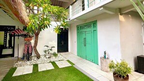 A courtyard with a thatched roof, a green door, and a potted plant.