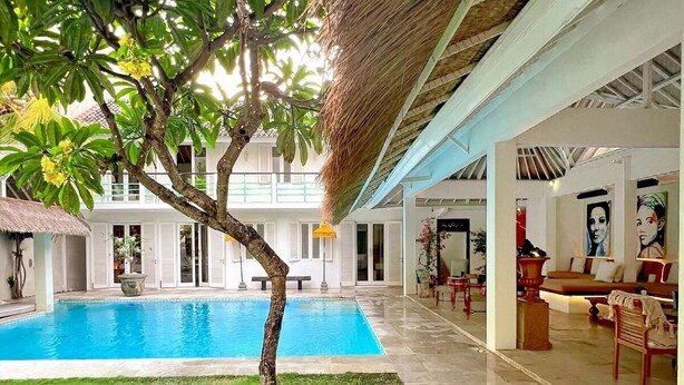 A pool area with a tree, a thatched roof, and a seating area with artwork.